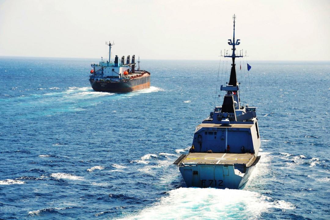Merchant vessel transiting under naval escort in a high-risk maritime corridor